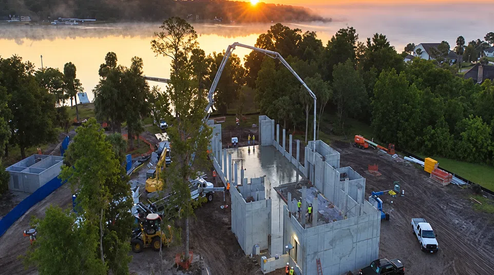Sunset over a lakeside construction site with concrete walls, workers, and machinery in progress.
