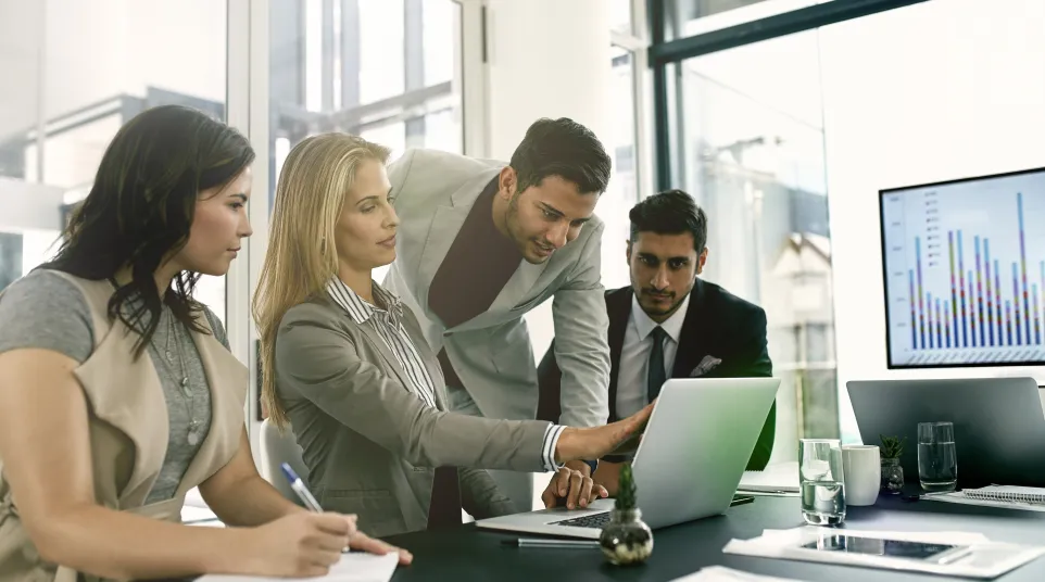 Business meeting with professionals discussing strategy around a laptop.