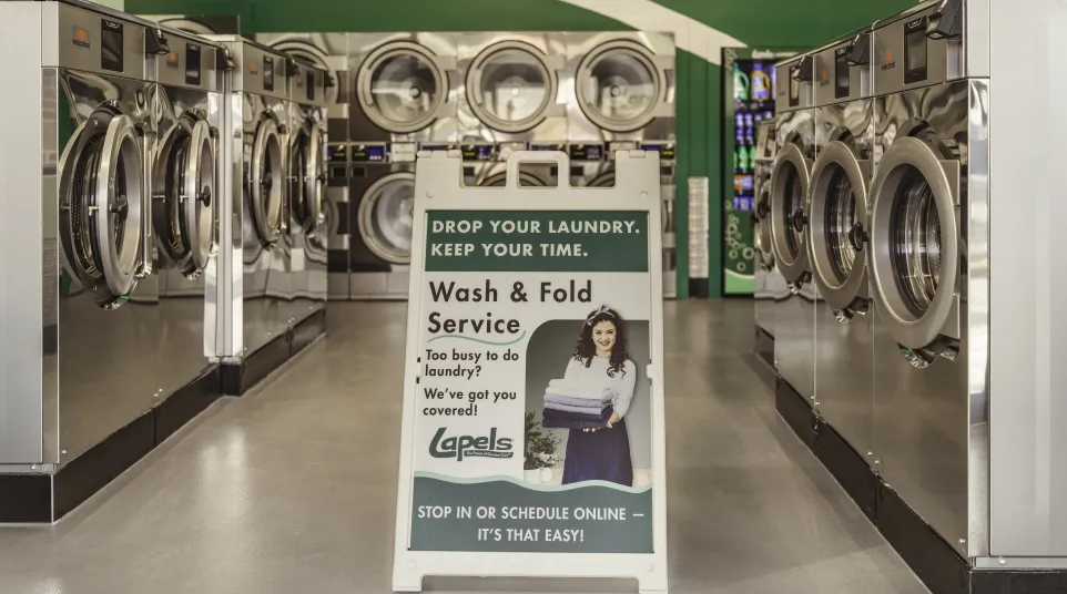 Interior of laundromat with rows of washing machines and a sign advertising wash and fold service.
