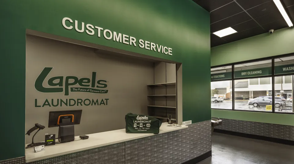 Customer service counter inside Lapels Laundromat with branded wall, computer, and green interior walls.