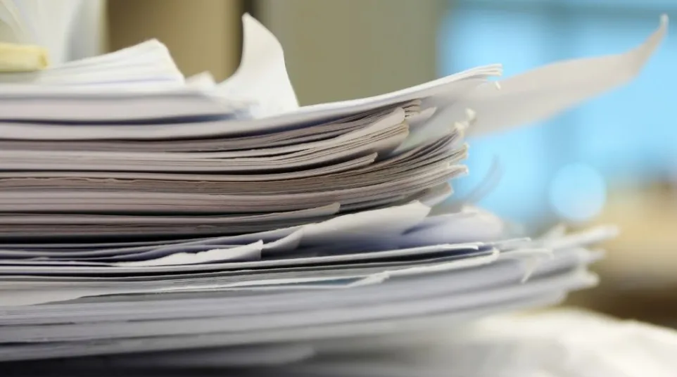 Close-up of a large stack of disorganized papers with blurred background in an office setting