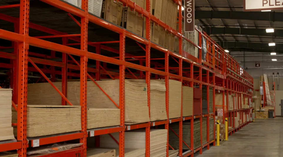 Warehouse storage racks filled with plywood sheets and boxes in an organized industrial facility interior.