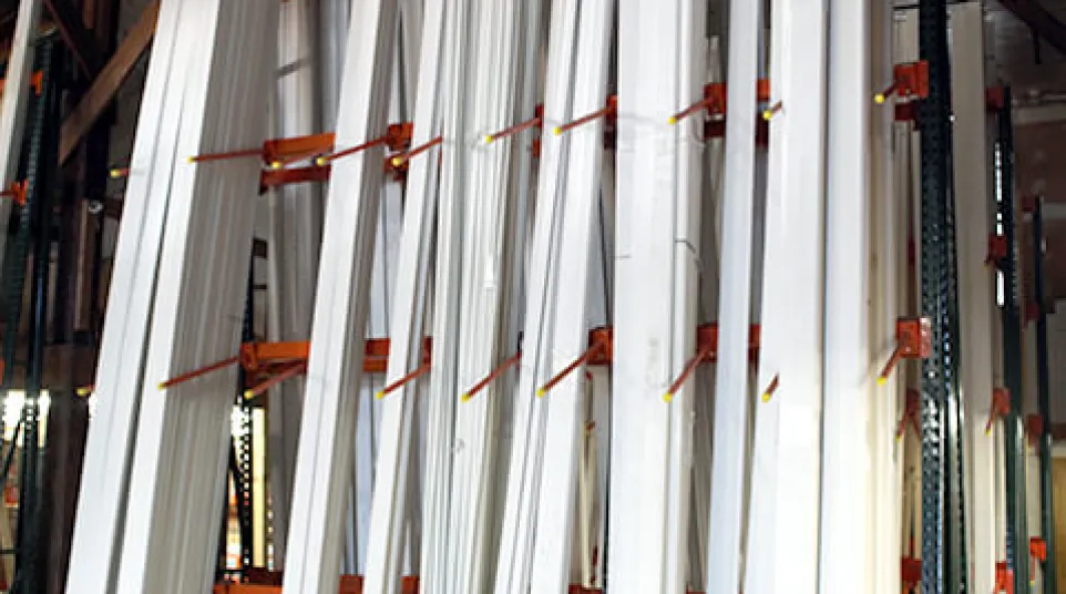 Stacks of white wooden trim pieces stored vertically on orange racks in a warehouse with industrial ceiling.