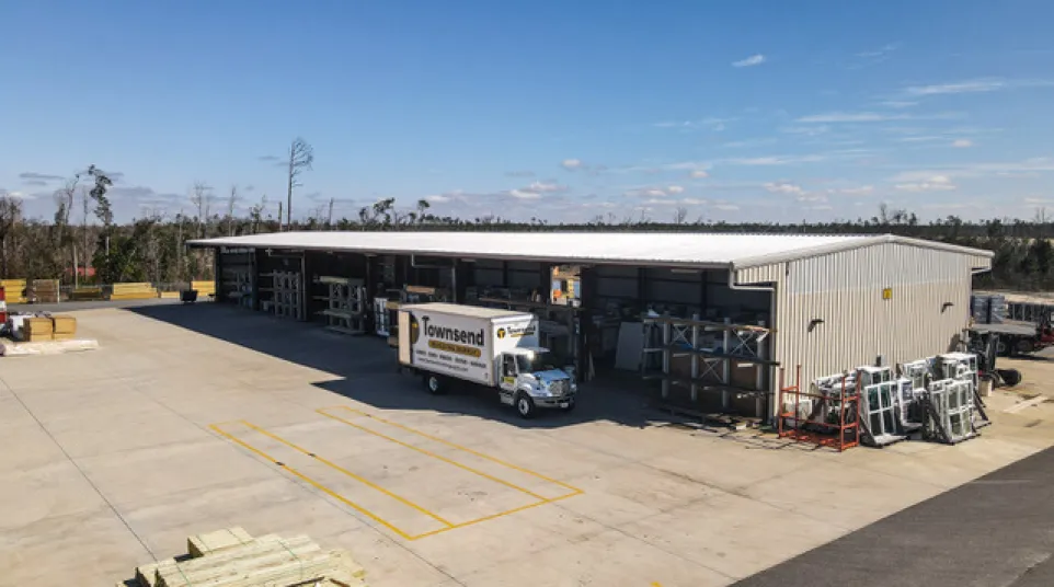 Warehouse with a Townsend delivery truck parked outside under a clear blue sky, surrounded by building materials.