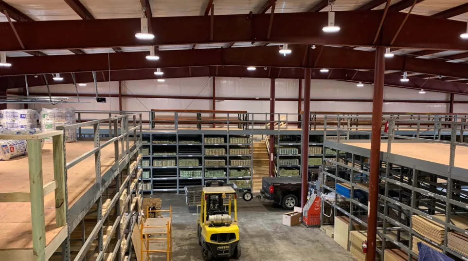 Interior view of a warehouse with metal shelving, a yellow forklift, and stacked inventory under bright lights