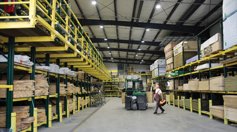 Spacious warehouse with organized shelves of lumber and a forklift operator walking across the floor
