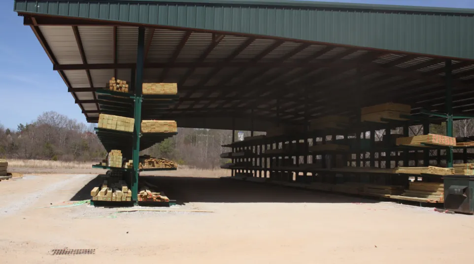Large open lumber storage shed with stacked wood planks under a metal roof on a clear day