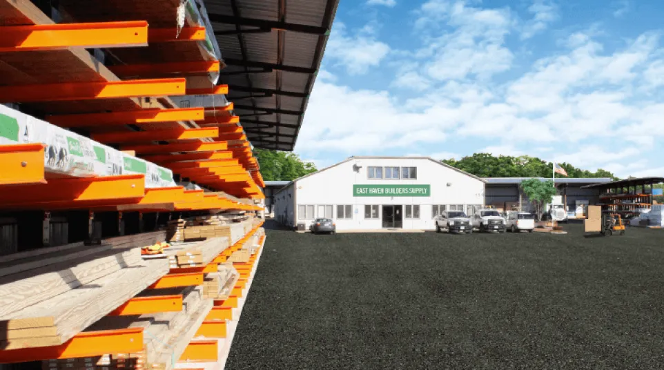 Outdoor lumber yard with stacks of wood on orange racks beside a white building labeled East Town Builders Supply.