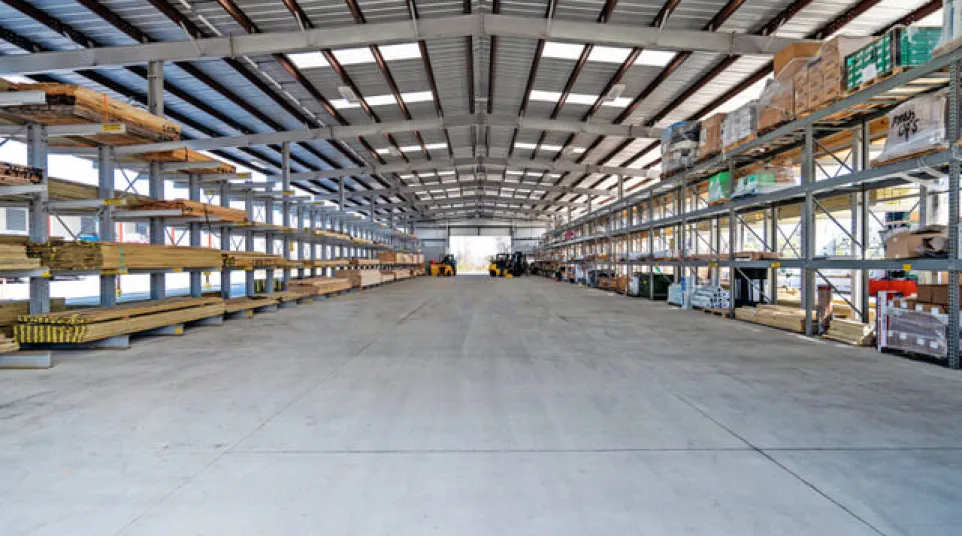 Spacious industrial warehouse with metal shelving stocked with building materials and clear concrete floor.