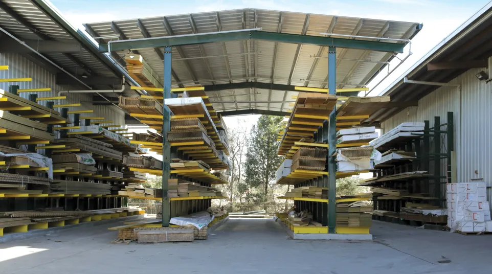 Outdoor lumber storage with wooden planks on metal shelves against clear sky and distant mountains.