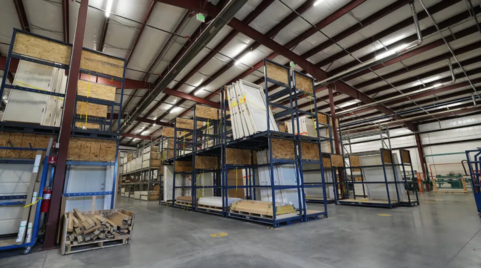 Spacious warehouse interior with metal shelving units storing wood panels and materials under bright ceiling lights.
