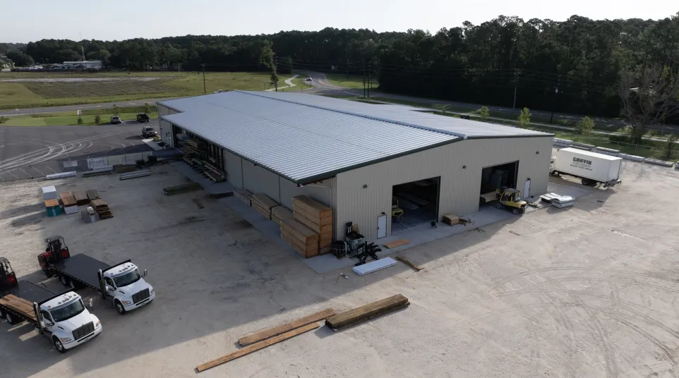 Aerial view of a large industrial warehouse with trucks, forklifts, and stacks of lumber on-site.