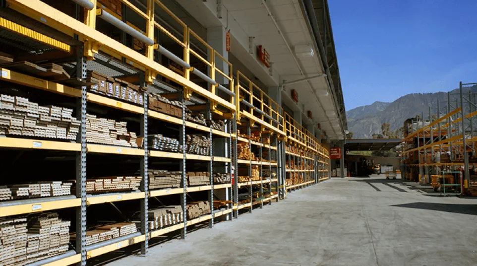 Outdoor lumber storage with wooden planks on metal shelves against clear sky and distant mountains.
