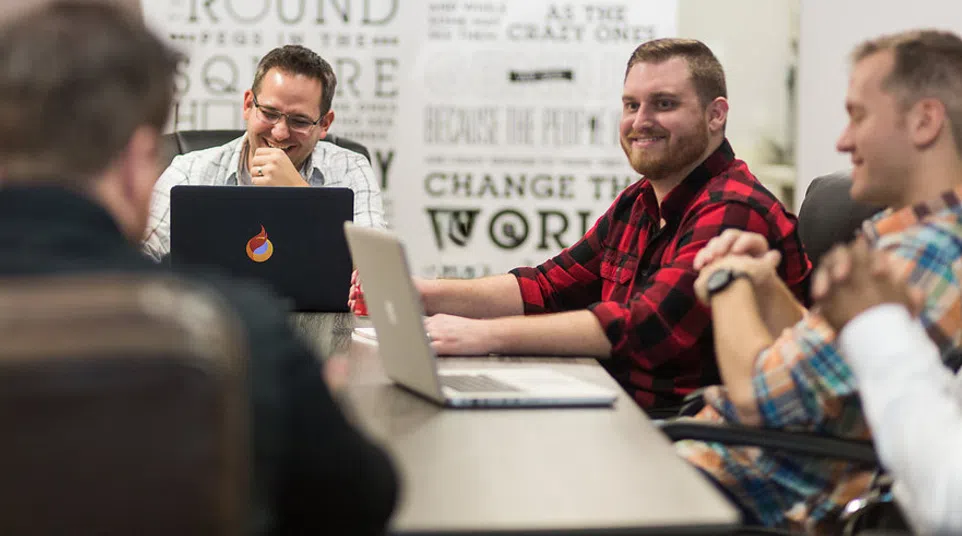 Four men having a meeting around a table with laptops in a modern office setting with motivational wall art.