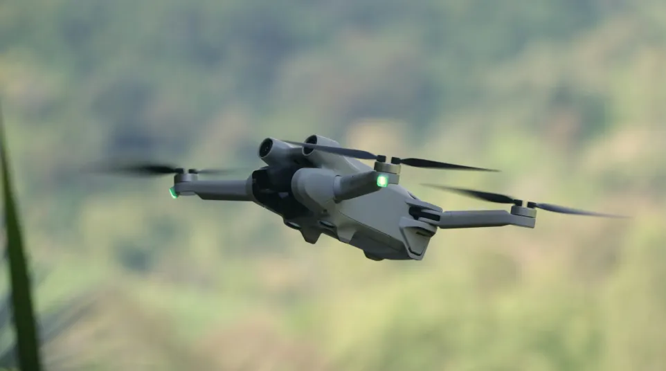 Close-up of a modern drone with spinning propellers flying outdoors against a blurred natural background