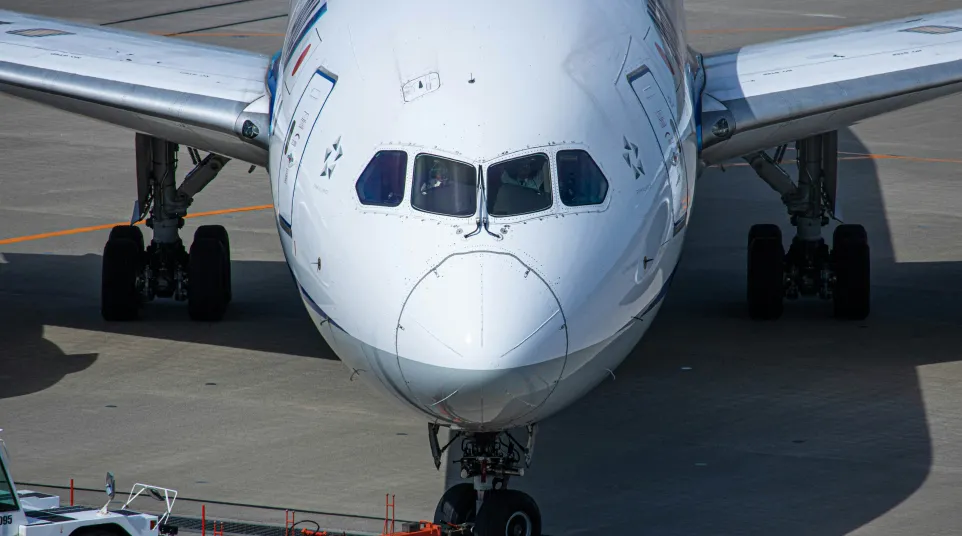 Close-up front view of a large commercial airplane on the runway with attached tow vehicle.