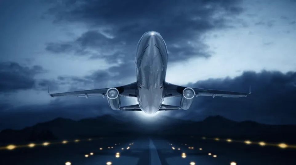 Aircraft taking off at night against a dramatic sky, illuminated runway lights in foreground.