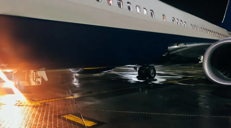 Close-up of airplane fuselage and engine on wet tarmac at night with glowing light reflections on surface