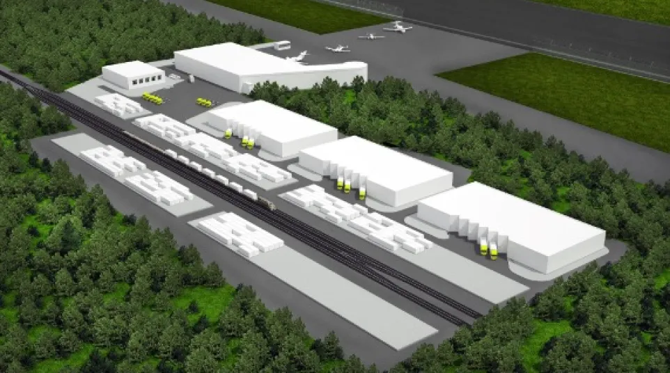 Aerial view of an industrial complex with warehouses, rail tracks, and airplanes near a runway surrounded by forest.