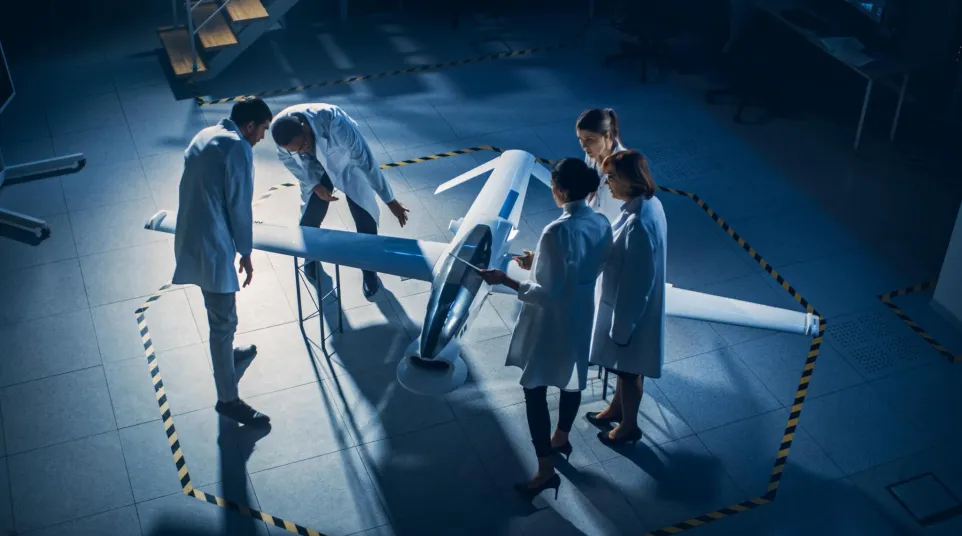 Four engineers in lab coats examining a sleek small aircraft prototype in a dimly lit hangar.