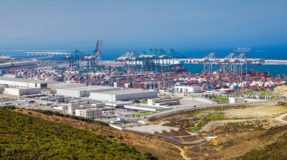 Aerial view of a busy shipping port with numerous containers, cranes, and industrial buildings by the sea.