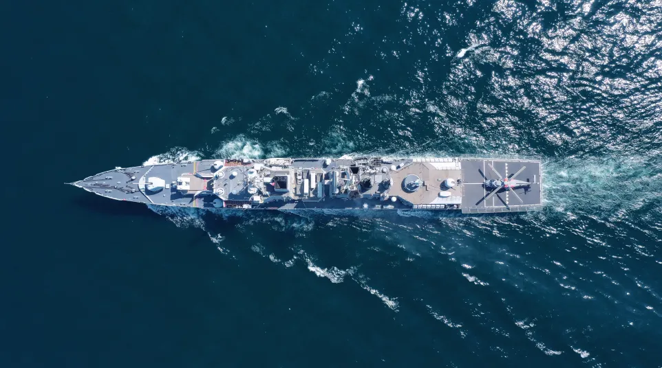 Aerial view of a large military ship sailing through deep blue ocean waters during daytime.
