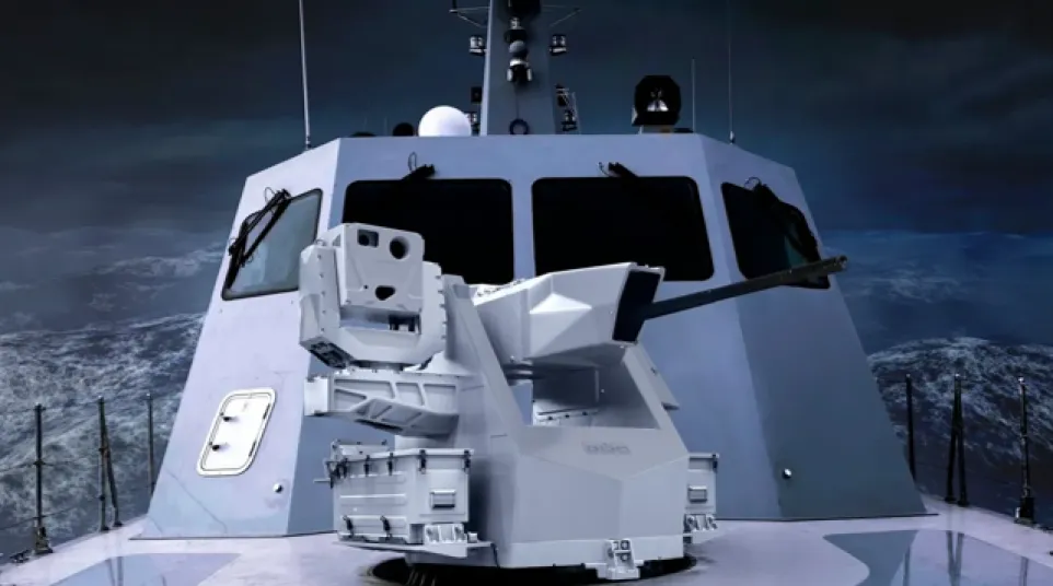 Modern naval gun turret mounted on a warship deck with stormy ocean background at dusk.
