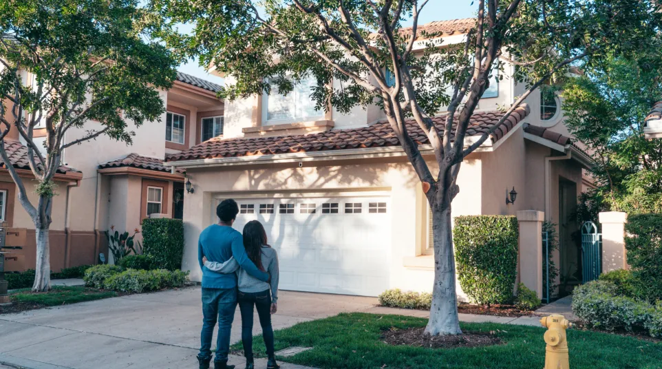 Couple admiring a beautiful suburban home with lush greenery and a welcoming exterior.