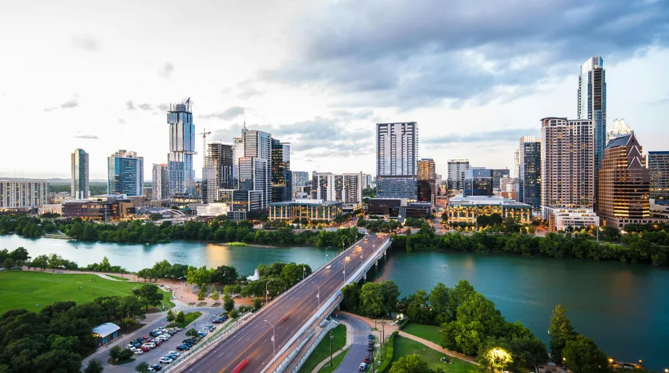 Panoramic view of Austin skyline with bridges and river under a cloudy sky during golden hour.