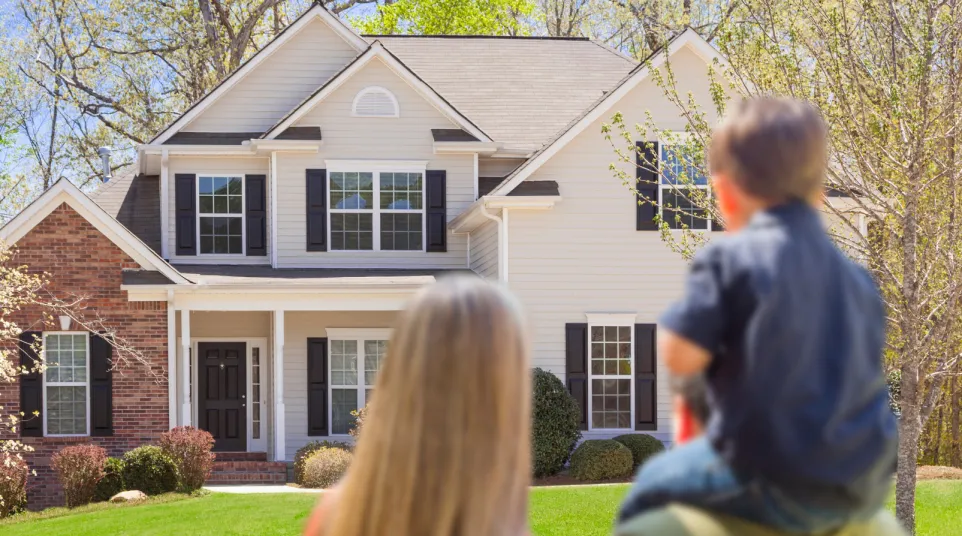 Family enjoying a sunny day in front of a beautiful suburban home with lush greenery.