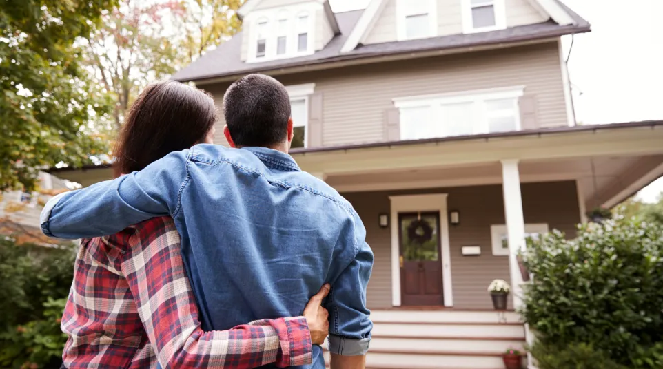 Couple admiring their new home with a welcoming porch and lush greenery in front.
