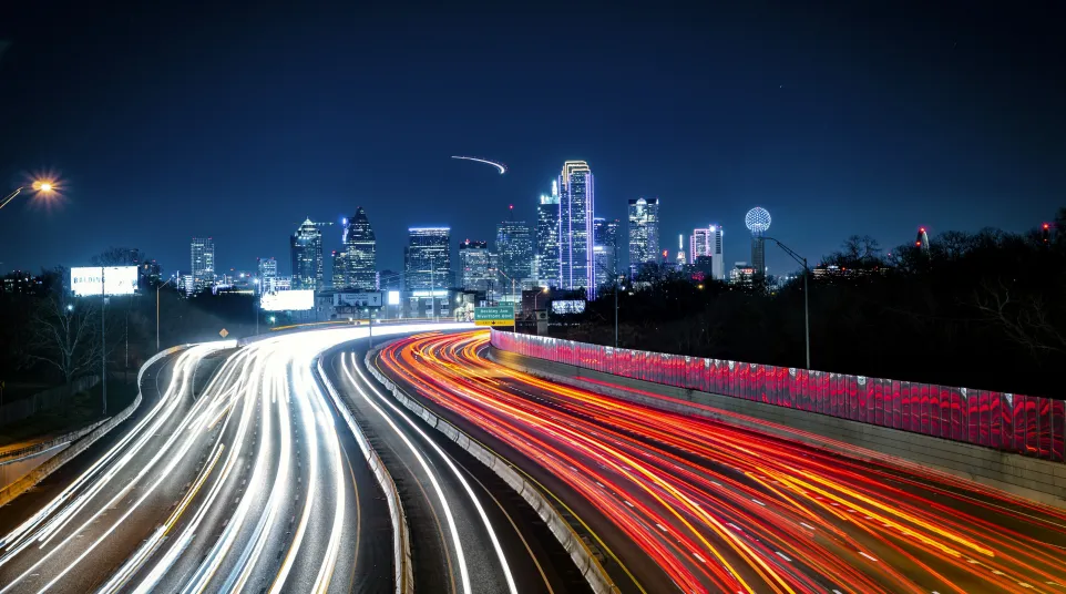 Dynamic light trails on a highway with a vibrant city skyline at night.