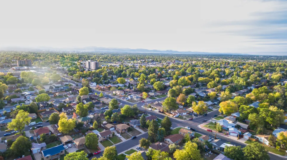 Aerial view of a vibrant suburban neighborhood with trees and homes under a clear sky.