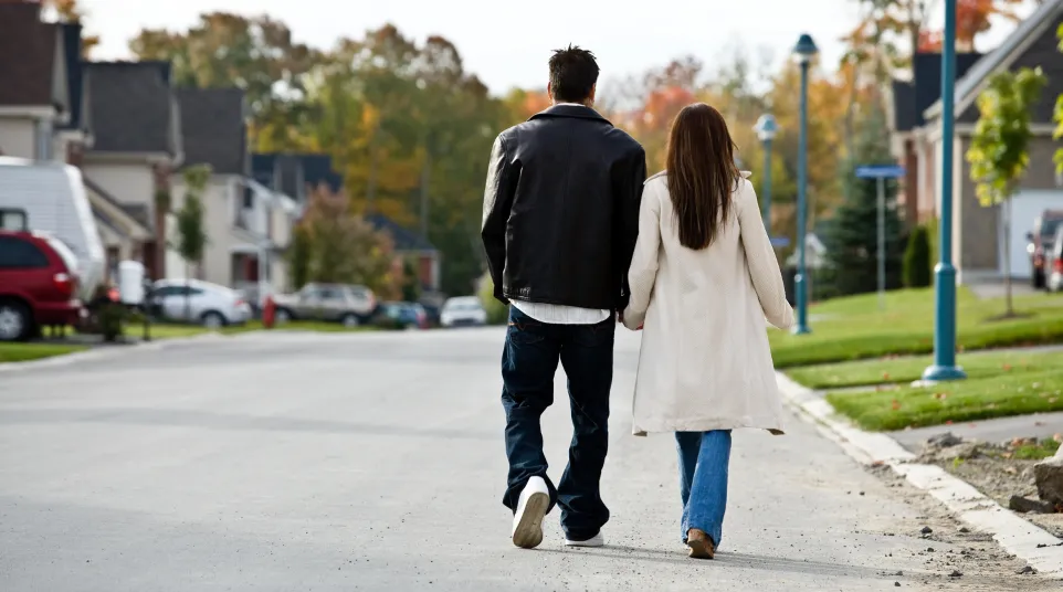 Couple walking hand in hand down a suburban street, surrounded by colorful autumn trees.