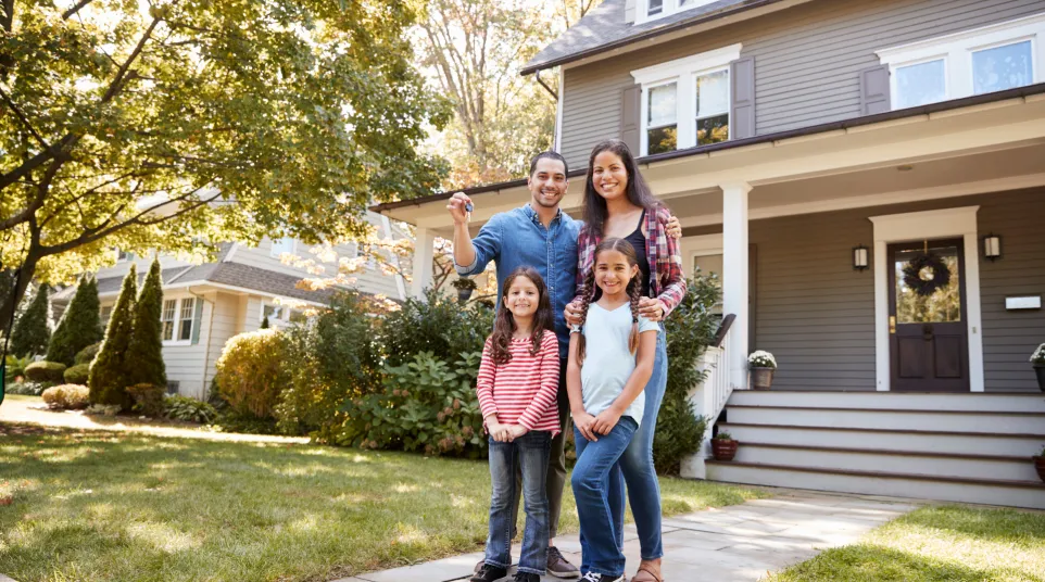 Happy family posing in front of their new home, showcasing joy and excitement of homeownership.