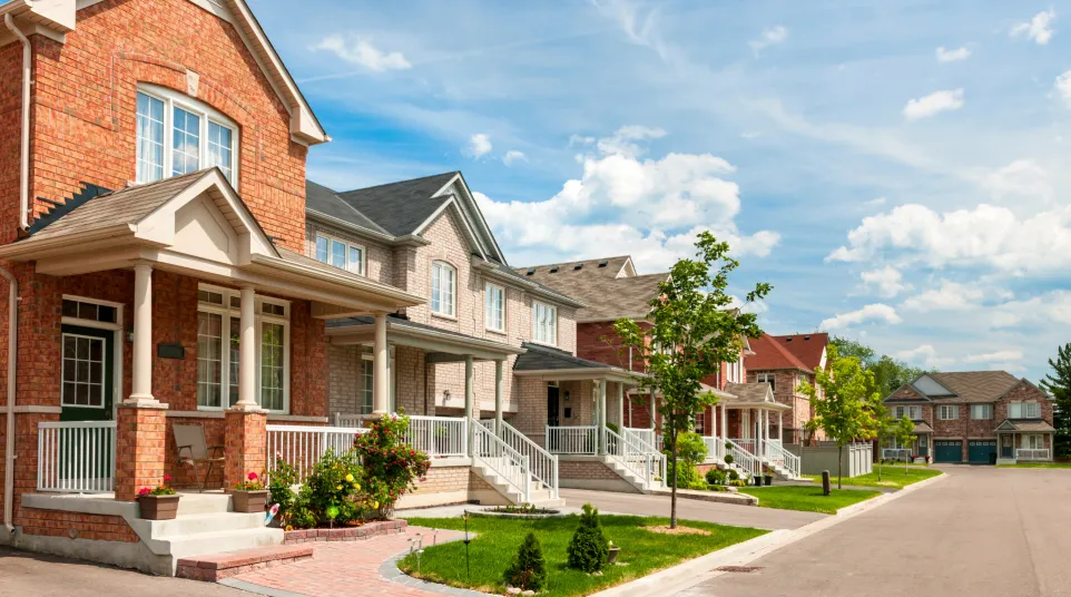 Row of modern suburban houses under a blue sky with scattered clouds, featuring lush green lawns.