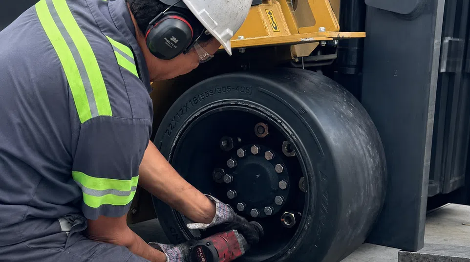 Worker in safety gear repairing or maintaining a heavy-duty forklift tire with power tool in industrial setting
