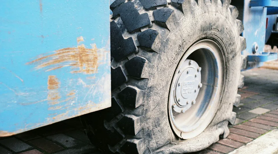 Close-up of a flat, worn-out tire on a blue industrial vehicle parked on a brick pavement.