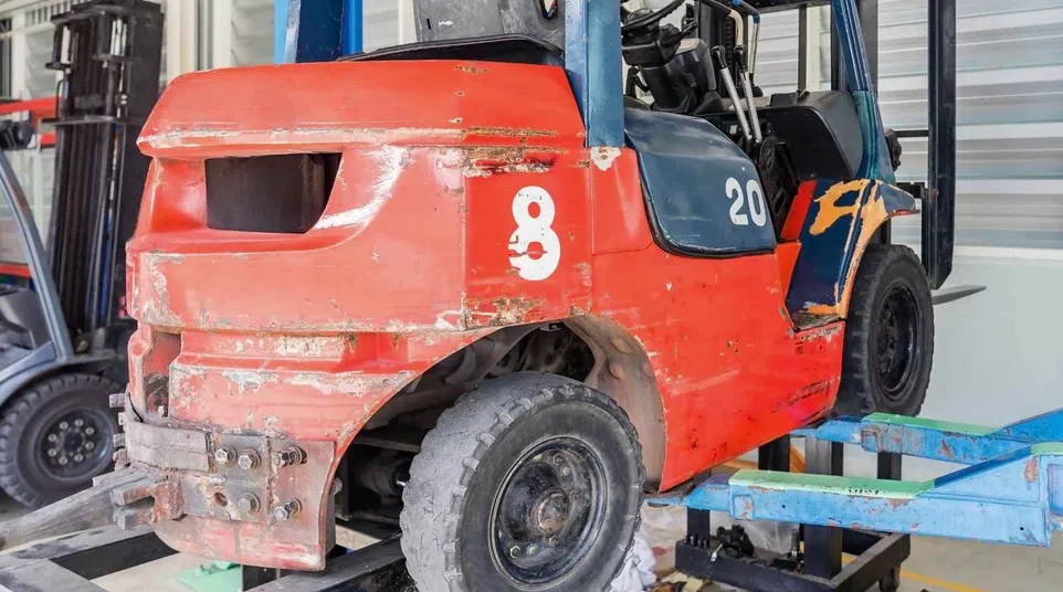 Close-up of a worn red and blue forklift in an industrial workshop during repair or maintenance work