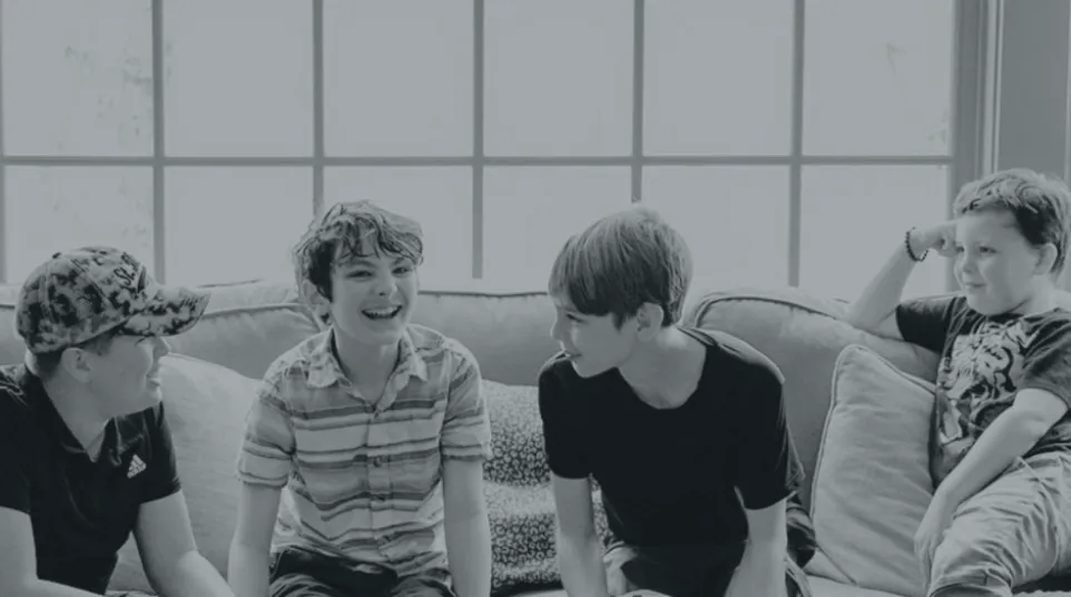 Four boys sitting and chatting on a couch in a bright living room with a coffee table in front of them