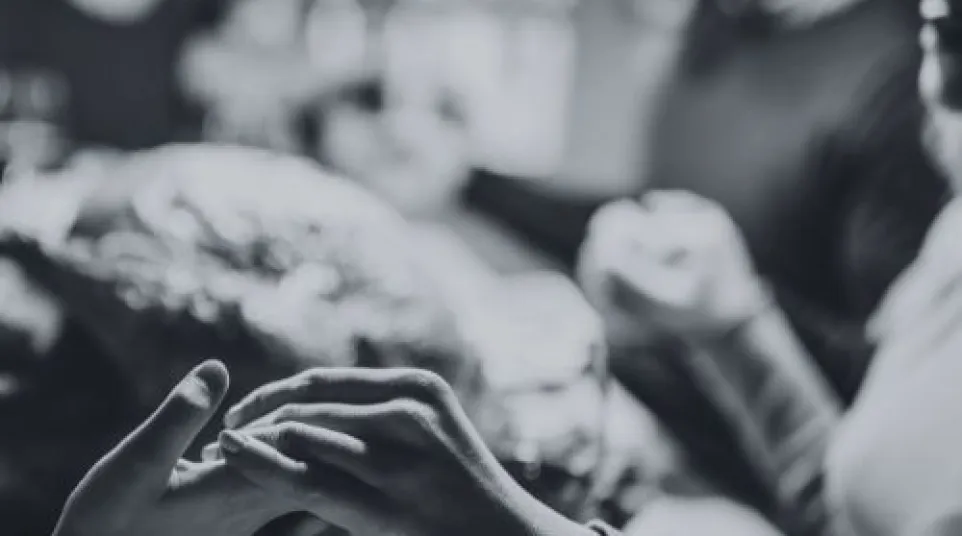 Black and white image of two people holding hands with blurred background at a social gathering.
