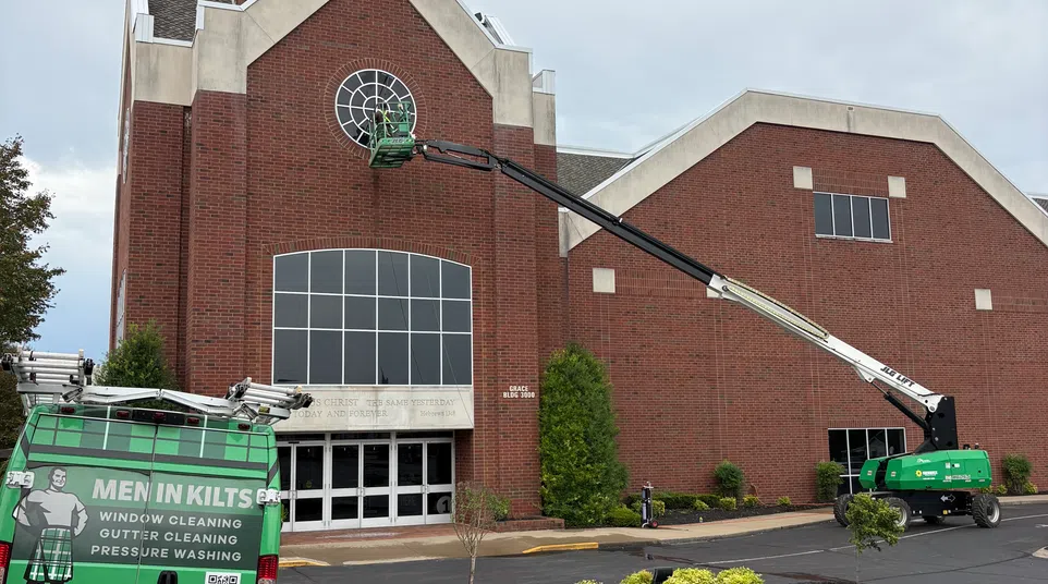 Men in Kilts cleaning windows on a church using a green lift and van in a parking lot with handicap spaces.