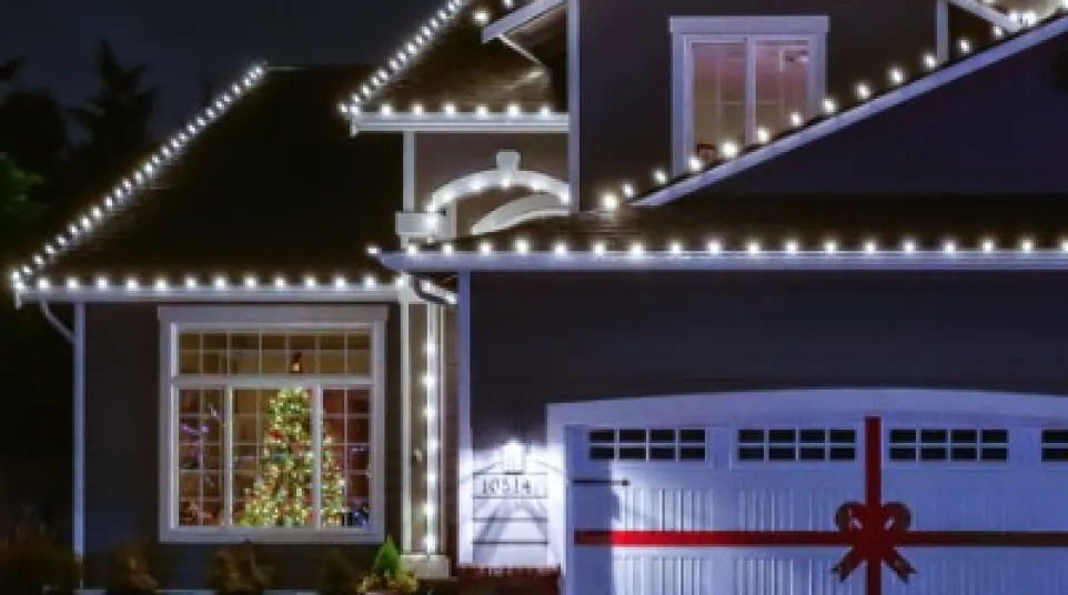 House decorated with white Christmas lights and a garage door wrapped like a gift with a red ribbon at night.