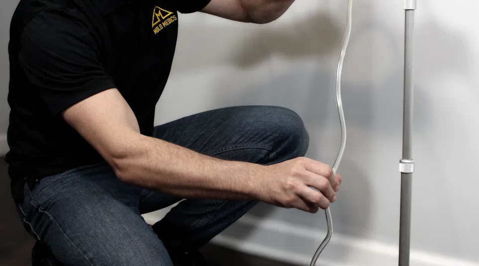 Technician in Mold Medics uniform setting up air sampling equipment in a room with hardwood flooring.