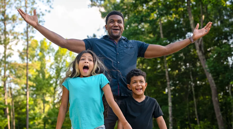 Happy man with two excited children outdoors surrounded by trees on a sunny day