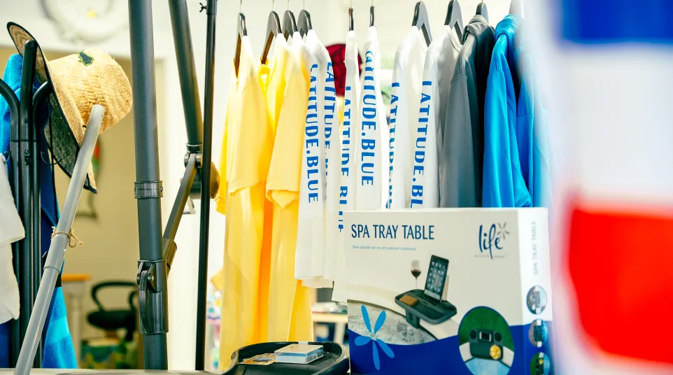 Colorful t-shirts hanging on rack with a boxed spa tray table and a straw hat in a bright indoor setting