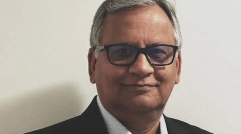 Middle-aged man with gray hair and glasses wearing a black blazer and light blue shirt against a white background