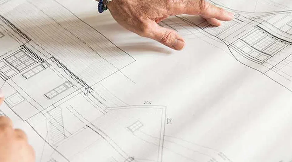Hand pointing to architectural blueprints of a house with detailed design and structural plans.