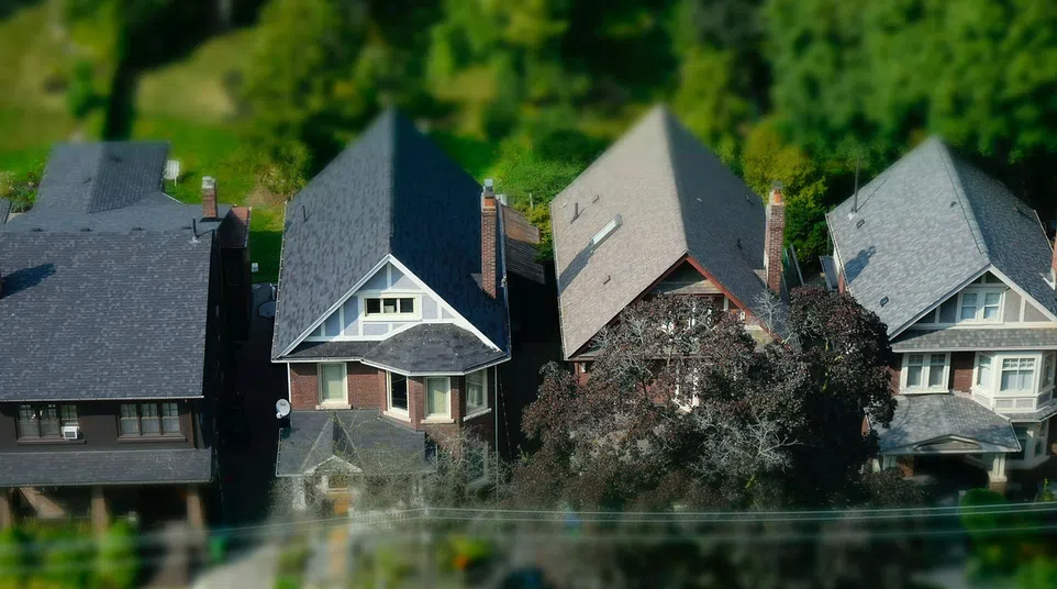 Aerial view of four closely spaced suburban houses with varied roof styles and greenery around.