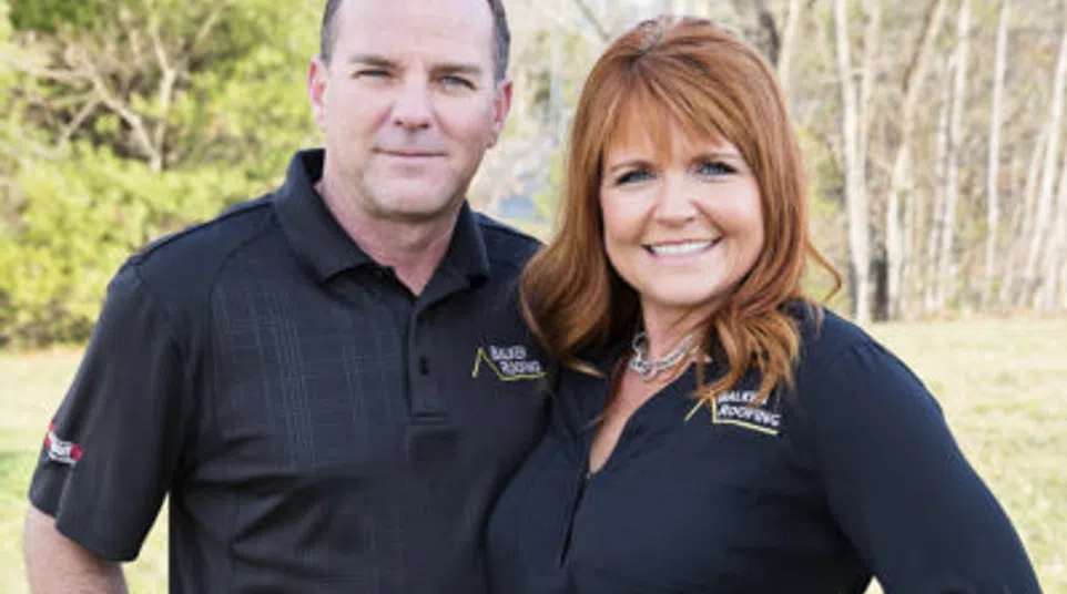 Man and woman standing outdoors in casual work attire smiling at the camera with greenery and trees in the background